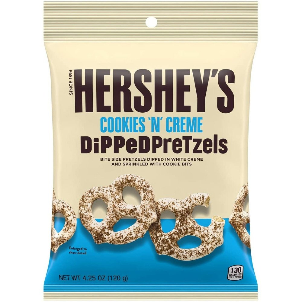Un emballage beige avec une bande bleu en bas, et des bretzels enrobés de chocolat blanc et saupoudrés poudre de cookies au chocolat, le tout sur fond blanc