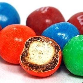 Des chocolats de couleur rouge, bleu, vert et orange sur fond blanc avec un orange en premier plan qui est coupé et on y voit une biscuit à l’intérieur