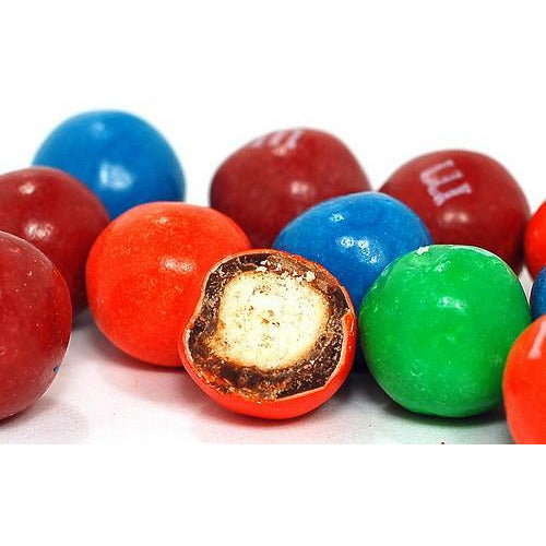 Plusieurs M&M’s bleu, rouge et vert. Et au centre un M&M’s orange coupé en 2, le tout sur fond blanc
