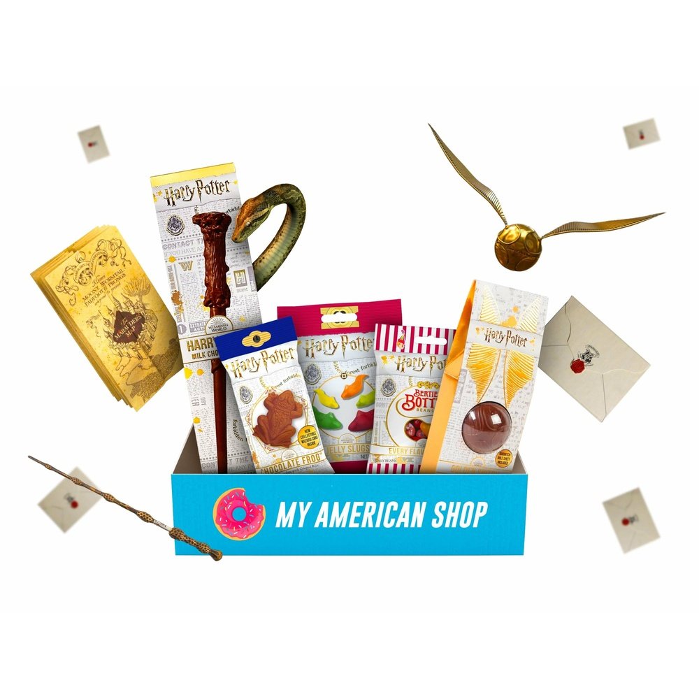 Un carton rectangulaire bleu sur fond blanc rempli de produits Harry Potter, bonbons et chocolat. Autour il y a des enveloppes blanches et Vif d’or, une petit balle avec des ailes en or