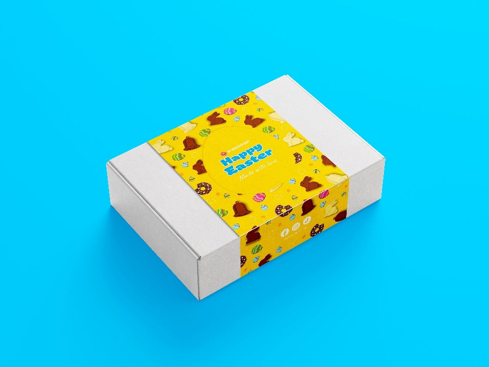 Un carton blanc sur fond bleu avec une partie jaune au centre avec des chocolat en forme de lapin, de cloches et des oeufs de Pâques colorés