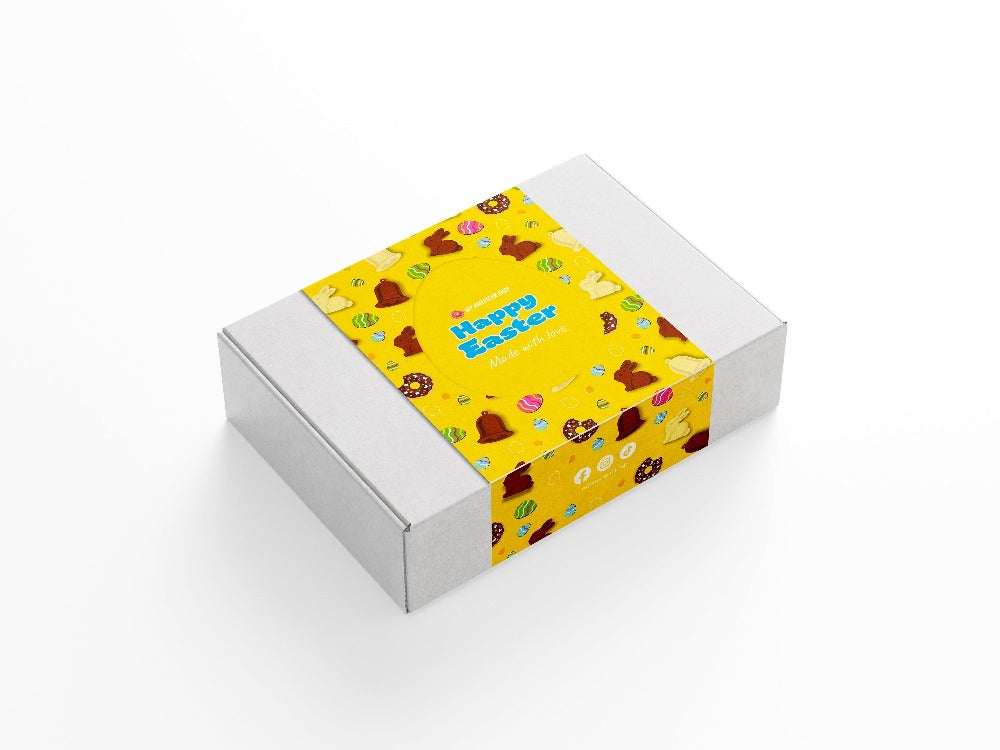 Un carton blanc sur fond blanc avec une partie jaune au centre avec des chocolat en forme de lapin, de cloches et des oeufs de Pâques colorés