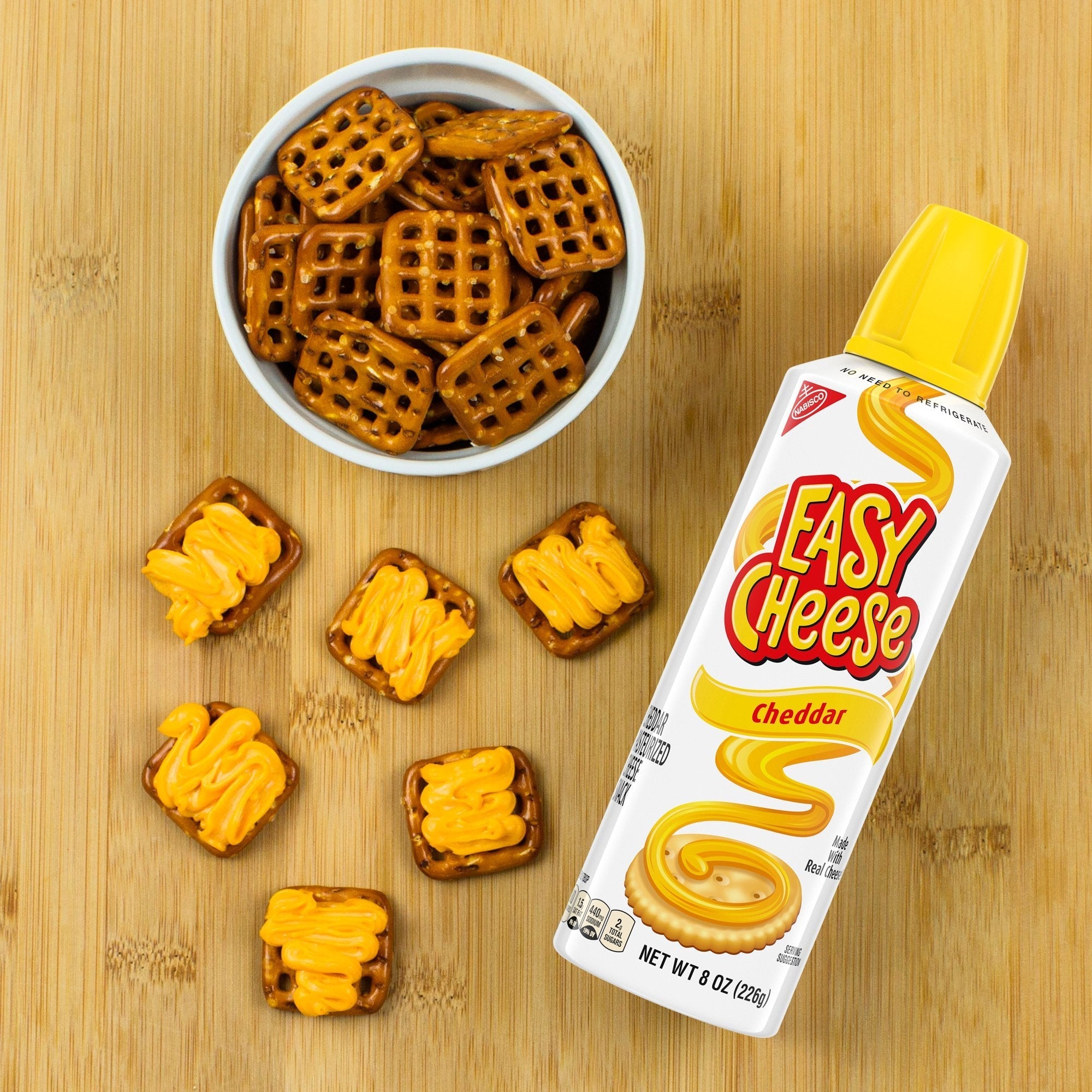 Un bol de bretzels et sur le devant plusieurs crackers de fromage en spray et à coté la bouteille blanche. Le tout sur une table en bois