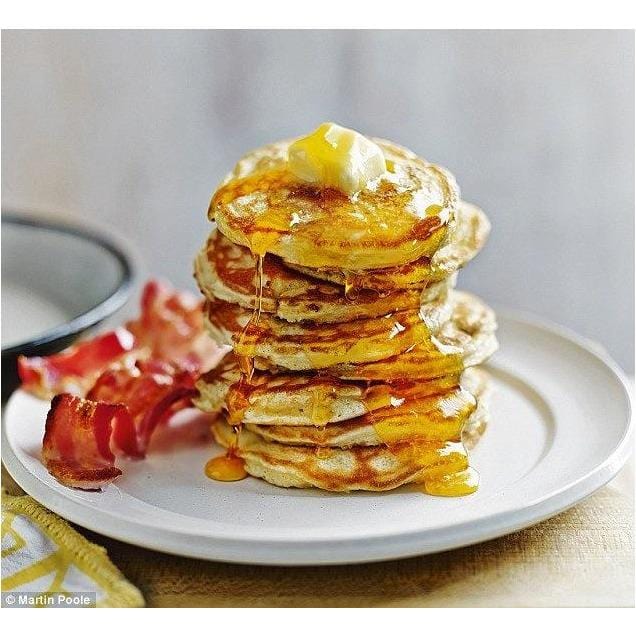 Une assiette blanche avec des pancakes, du sirop brun et du bacon. Le tout sur une table en bois