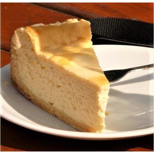 Une part de tarte et beaucoup de crème dans une assiette blanche avec un fourchette argenté, le tout sur une table en bois