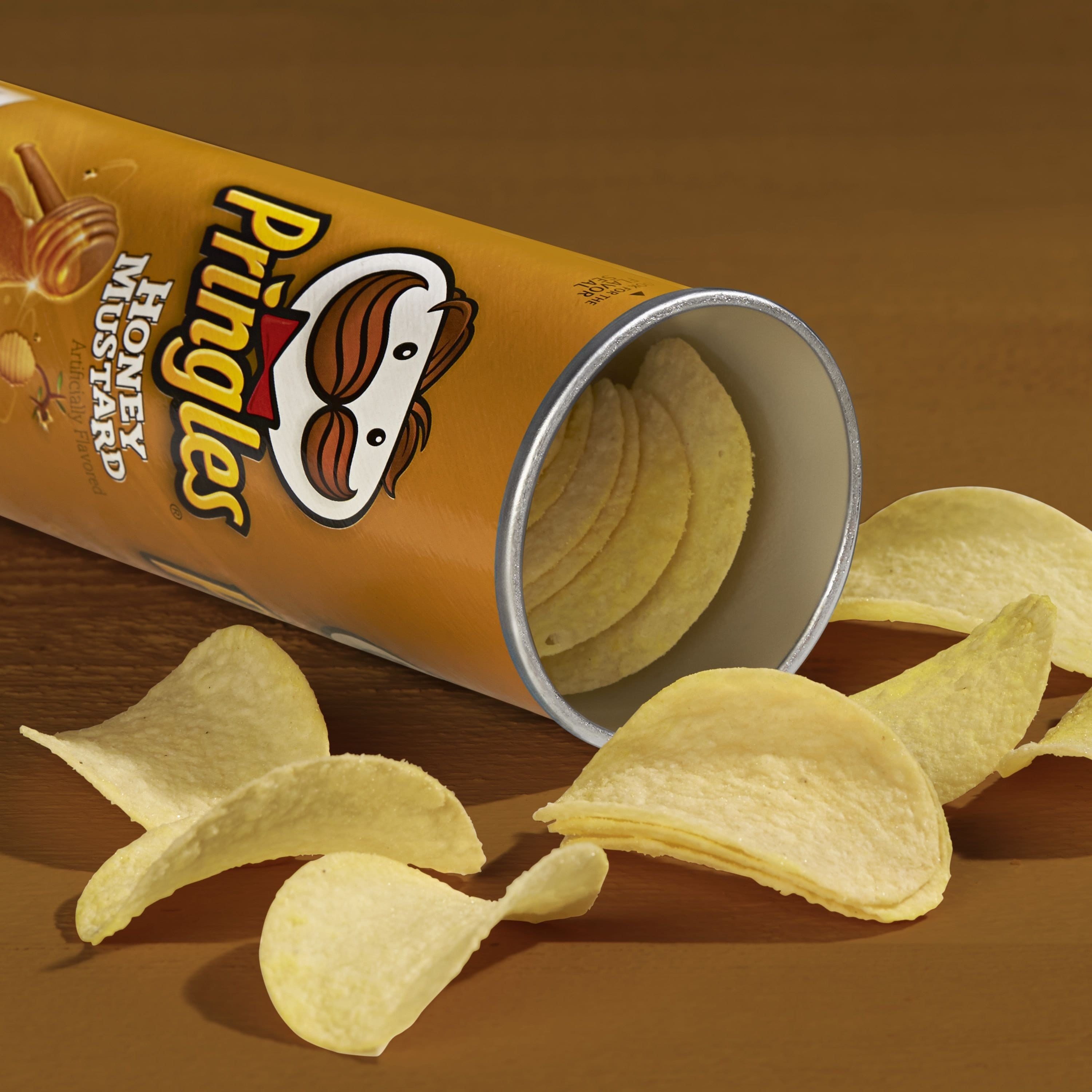 Un paquet en forme de cylindre brun clair ouvert, avec des chips jaunes qui sortent. Le tout sur une table brune